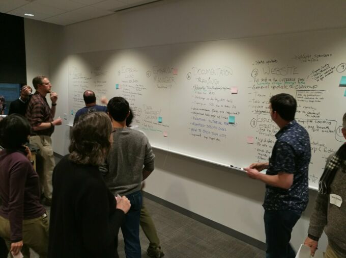 A group of scientists stand in front of a whiteboard and discuss Neotoma strategic priorities