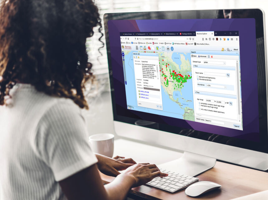 A woman standing in front of a large monitor with Neotoma Explorer data interface on her monitor